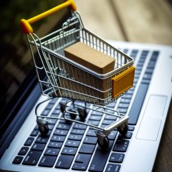 Small shopping cart sitting on top of laptop computer keyboard with cardboard box in the bottom of the cart. Generative AI.